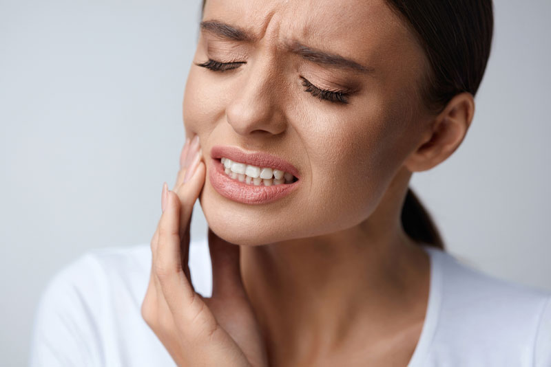 a woman holding her jaw in pain because she needs emergency dentistry