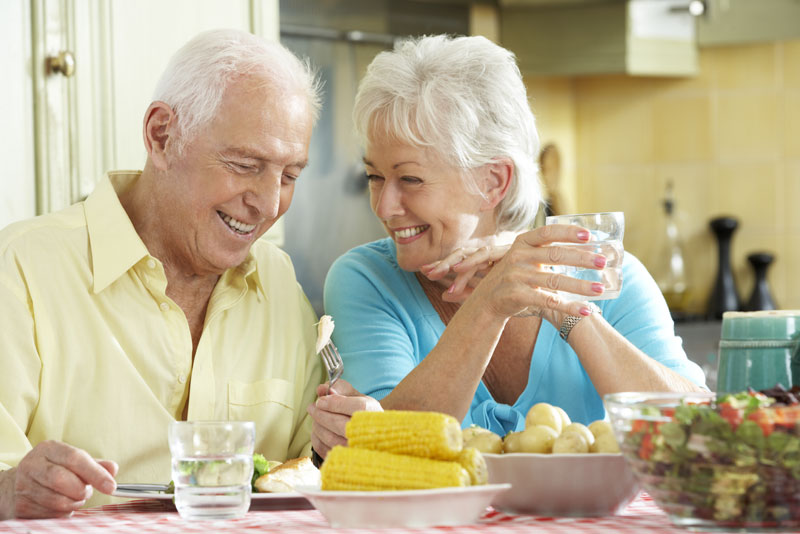 an elderly couple smiling at each other as they eat corn because they were able to get their dental implants accurately placed with advanced dental technologies.